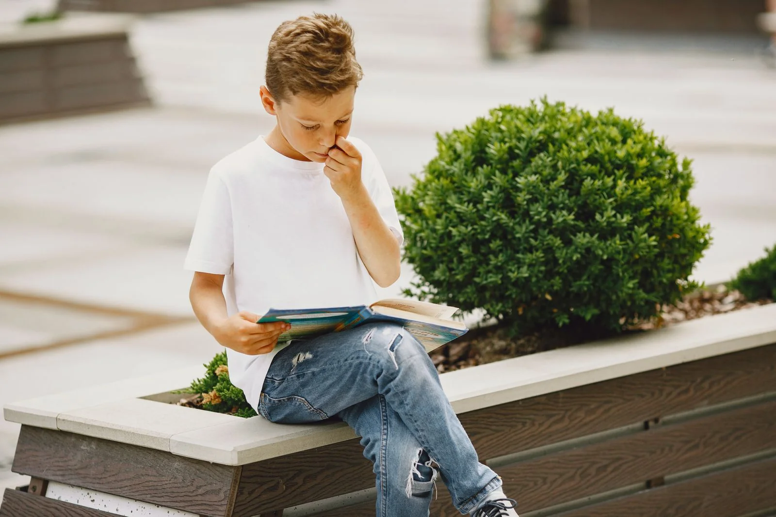 Jongen leest buiten een boek op een bankje