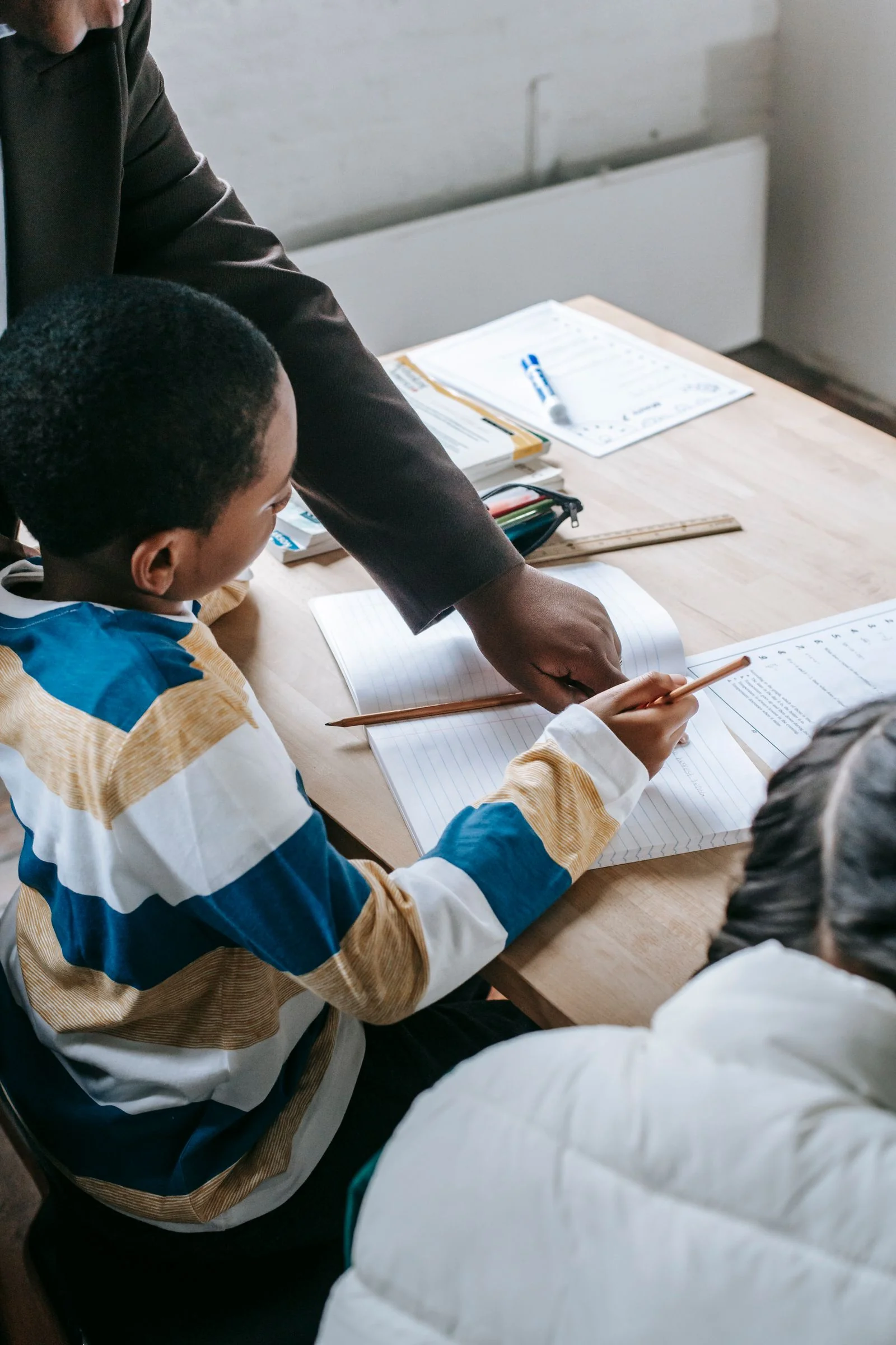 Leerkracht ondersteunt een kind bij schoolwerk aan tafel